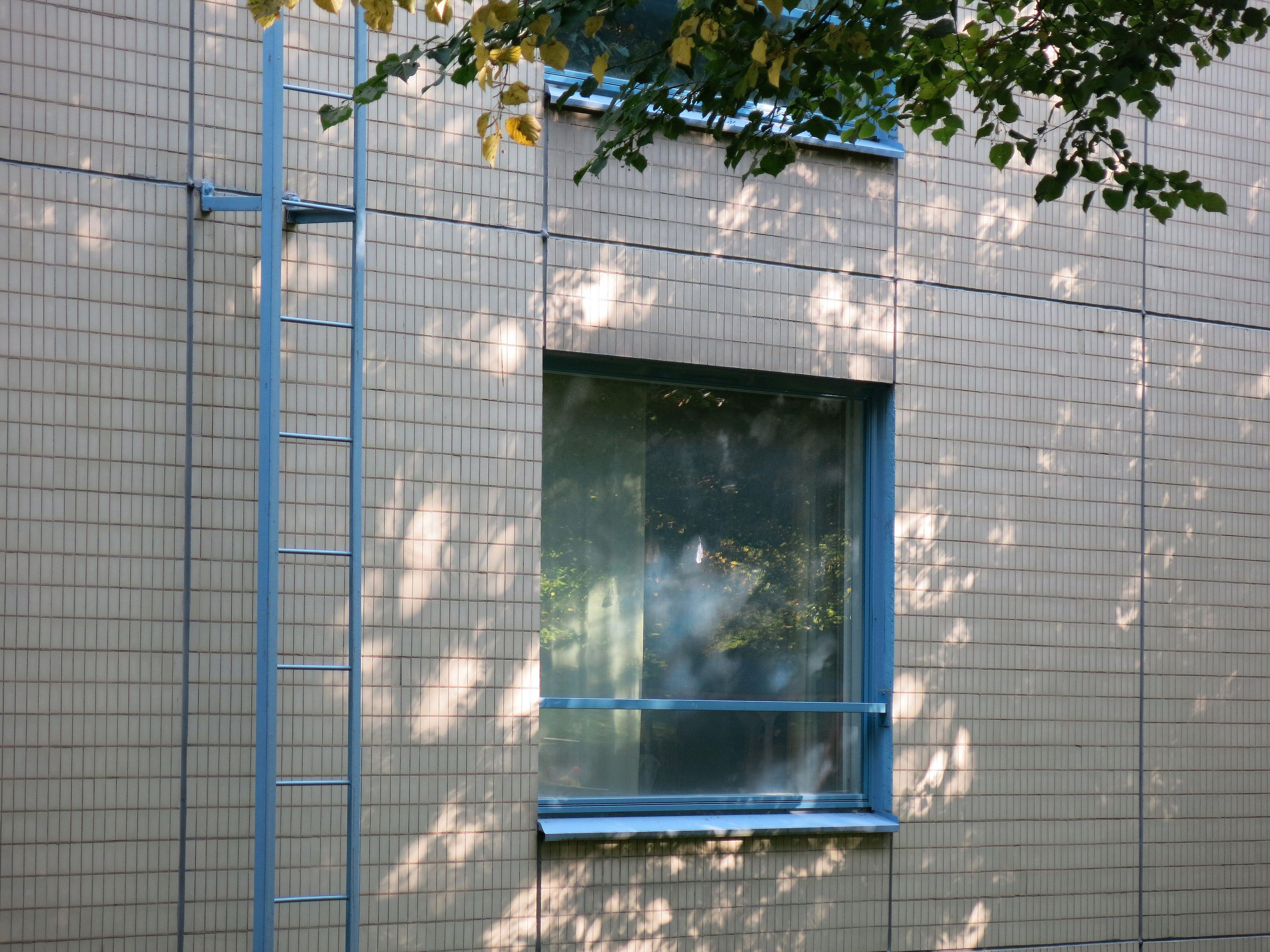 Elementtijulkisivu, jossa näkyy pienet vaaleat klinkkerilaatat, elementtisaumat sekä siniset ikkunapuitteet ja katolle johtavat kiinteät tikkaat.