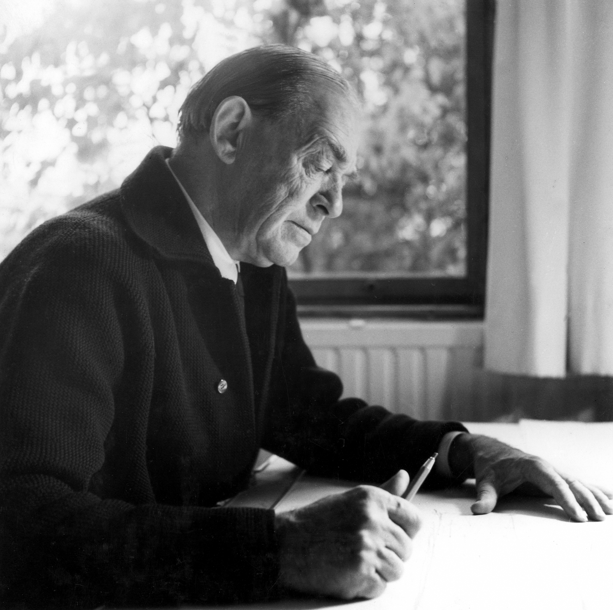 Alvar Aalto kuvattuna profiilista työpöytänsä ääressä.