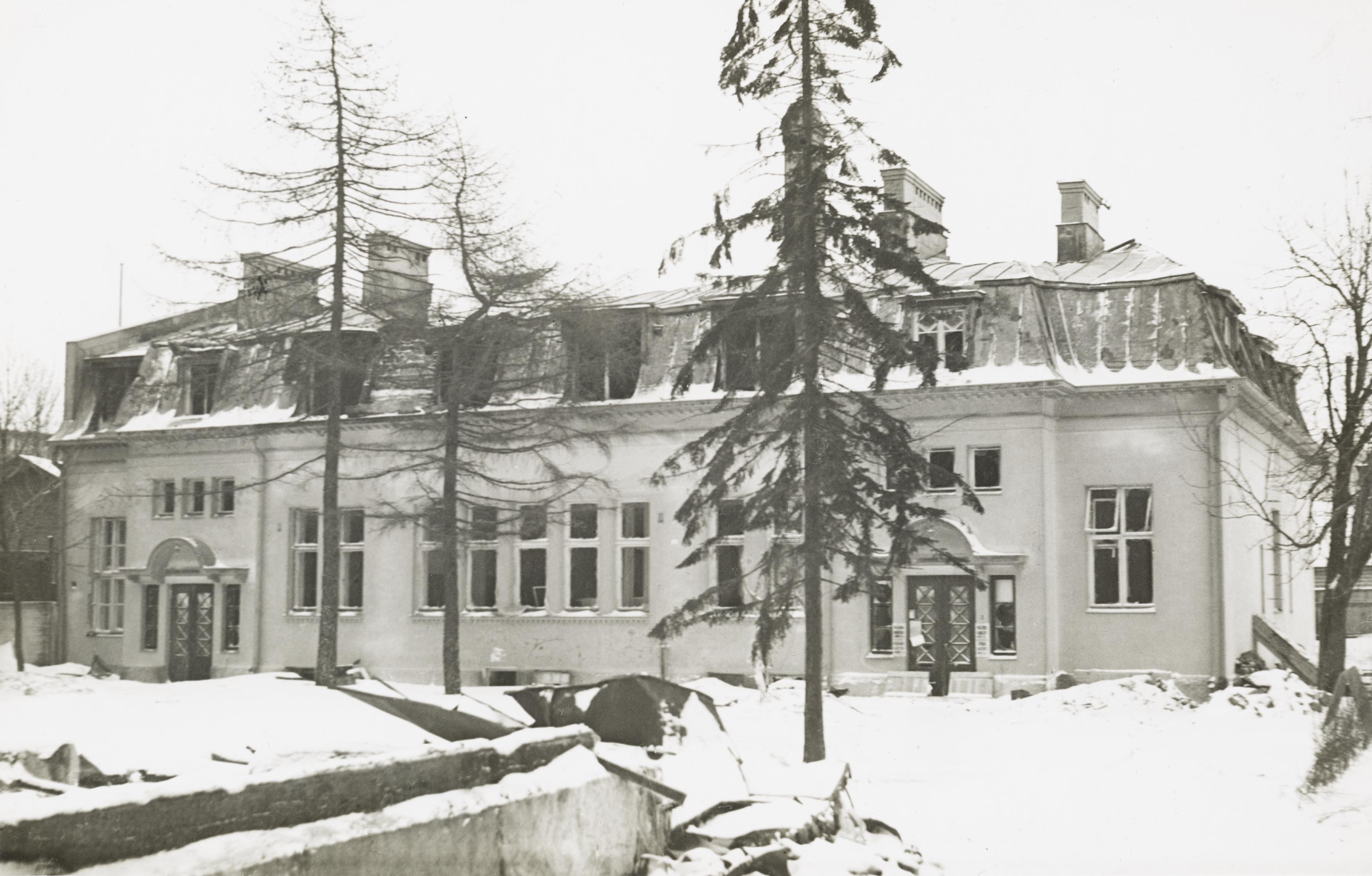 Mustavalkoisessa valokuvassa juuri valmistunut kaksikerroksinen, vaalea mansardikattoinen rakennus ja muutamia puita sekä lunta maassa.
