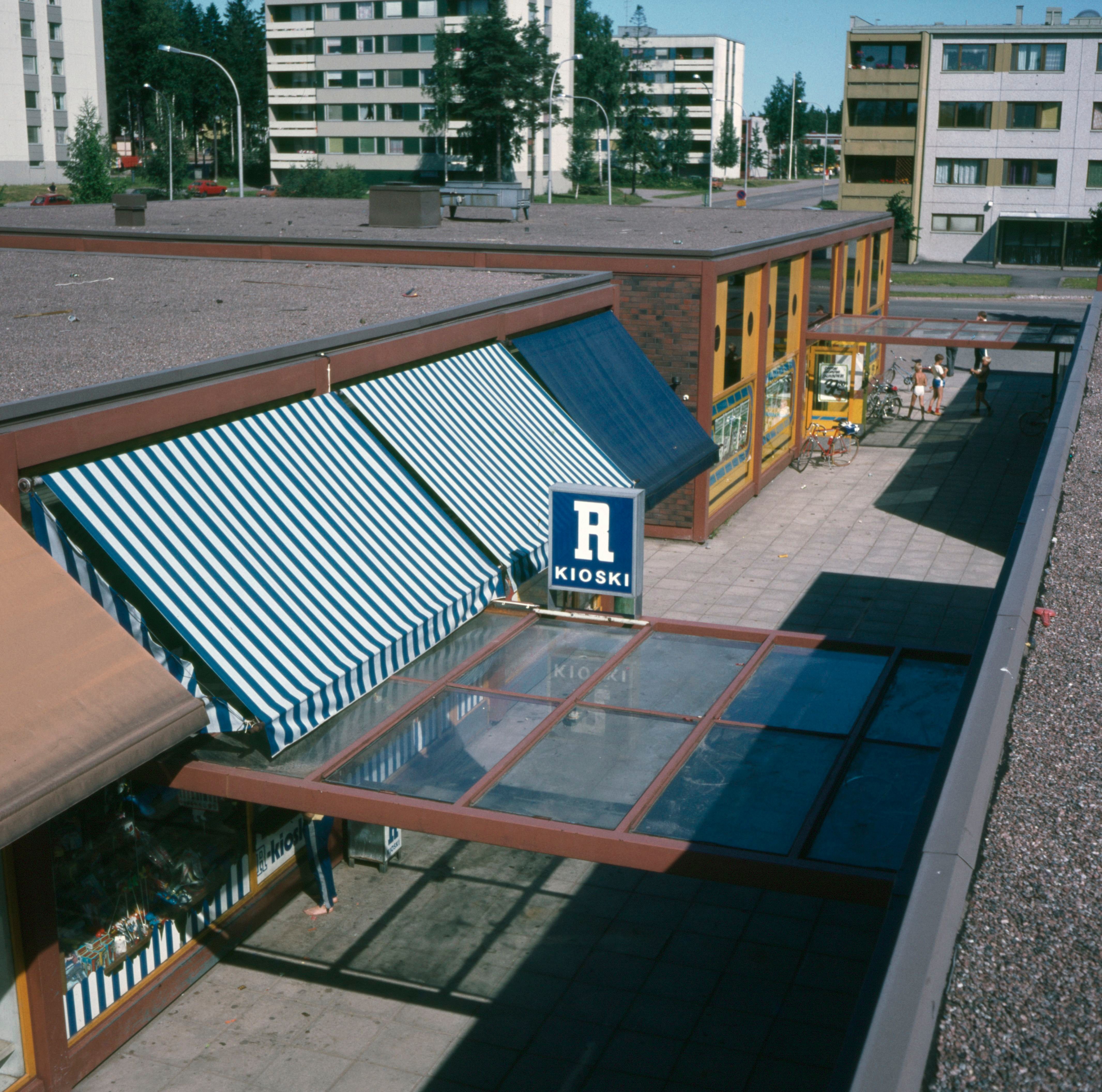 Matalan ostoskeskusrakennuksen katolta otettu valokuva rakennusosien rajaamalle, osin katetulle keskuskäytävälle, jonka varrella sijaitsee liiketiloja mm. R-kioski.
