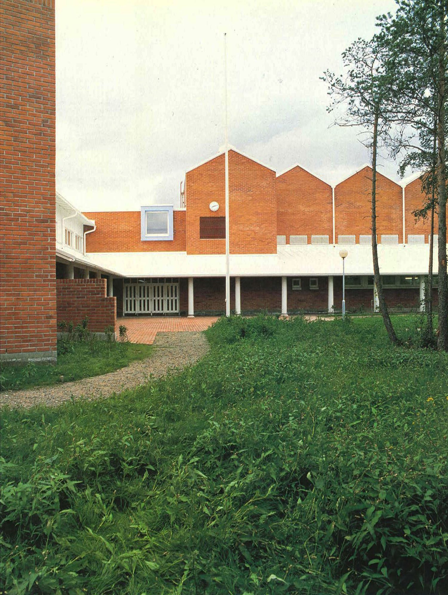 Koulun pääsisäänkäynti ja pitkä julkisivun suuntainen sisäänkäyntikatos. Julkisivut on muurattu punatiilestä.