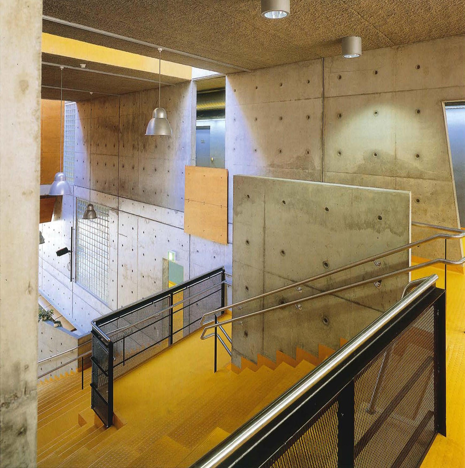 Koulun keskusaulassa sijaitseva auditorio, jonka eri tasanteet on erotettu teräsverkkokaiteilla. Keskusaulan seinät ovat maalaamatonta puhtaaksi valettua betonia.