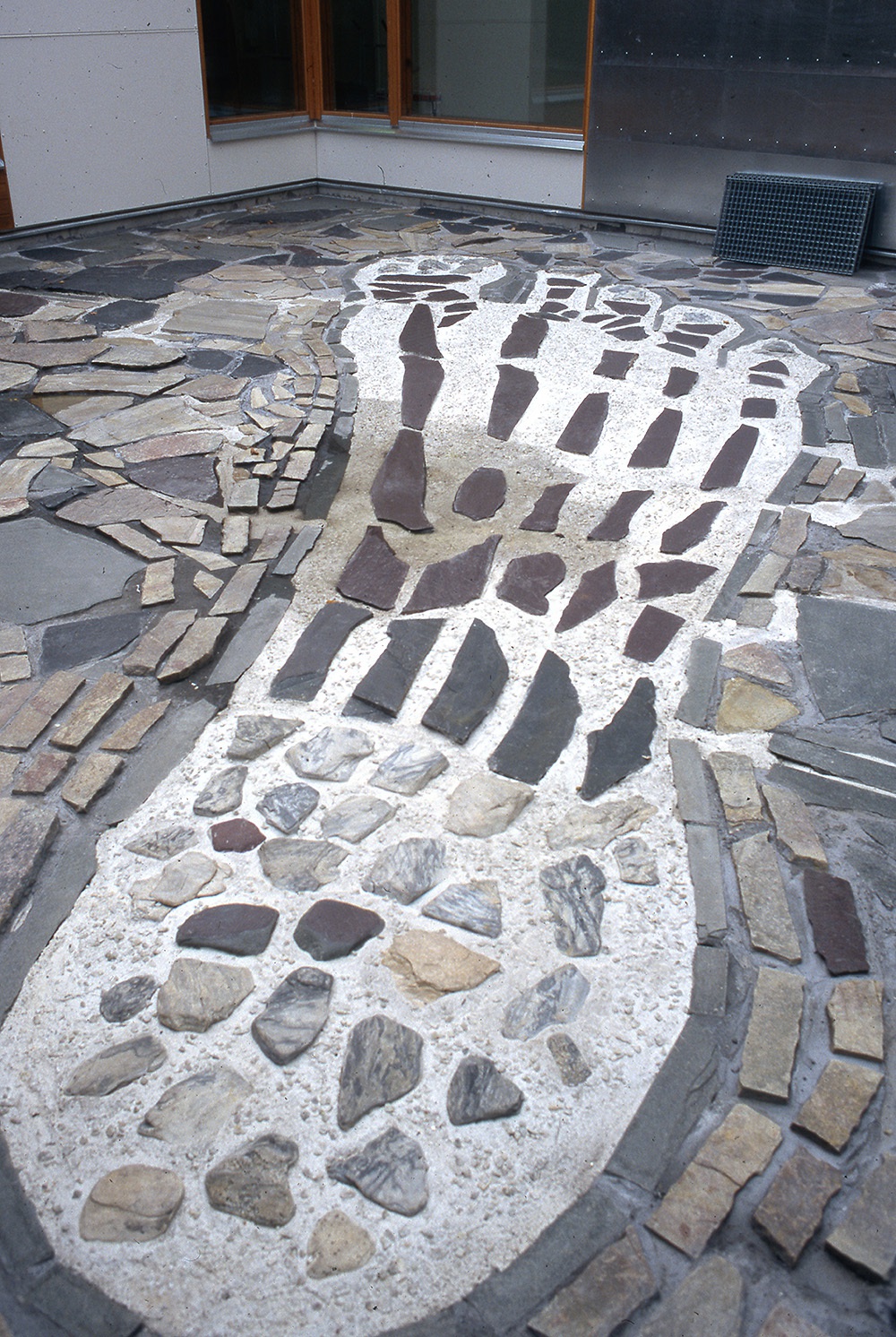Koulun kivetylle sisäpihalle taiteilija on kivilaatoista muotoillut suuren mosaiikkiteoksen, joka muistuttaa suurta jalanjälkeä.