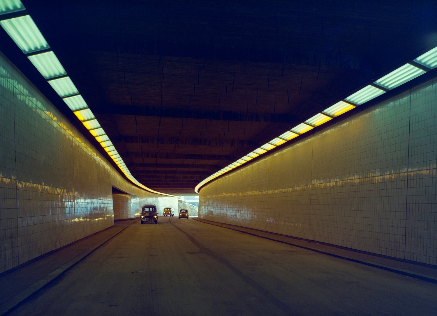 Näkymä tunnelista, jossa ajaa kolme autoa. Tunnelin seinät on päällystetty kiiltävillä kaakeleilla. Katon reunoilla on kaksi valaistusvyöhykettä.