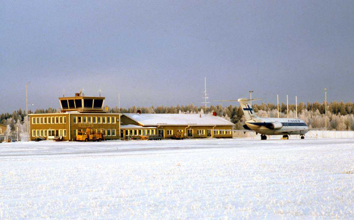 Talvinen näkymä kenttäalueen suunnasta lentokenttäterminaalille, joka on yksi- ja osin kaksikerroksinen rakennus. Kentällä seisoo lentokone.